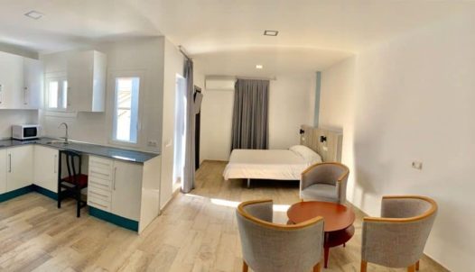 Habitación moderna y luminosa en Hotel Madrid Río con zona de cocina, cama confortable, sala de estar y tornos para viajeros que buscan comodidad en Madrid.