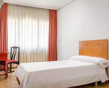 Habitación sencilla y luminosa en Hotel Madrid Río con cama individual, vista a la ventana con cortinas y mobiliario moderno.