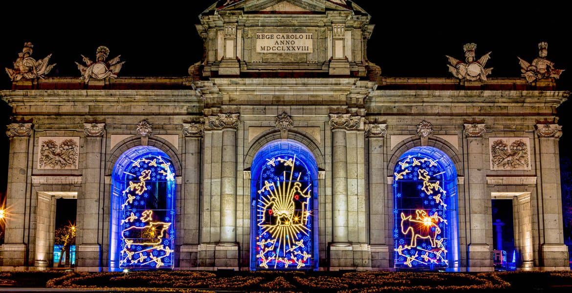 Brillante iluminación navideña en el Arco de la Victoria, Madrid, con decoraciones temáticas de Navidad en azul y amarillo.