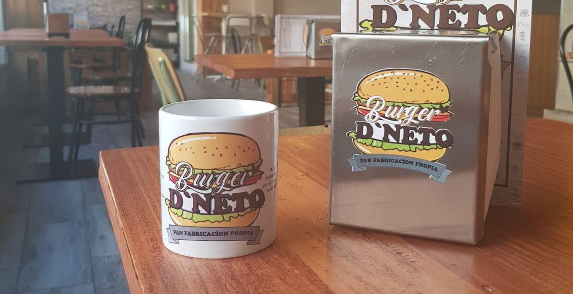 Hamburguesa y bebida con logotipo de Burger D'Neto en un restaurante.