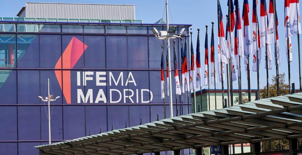 Fachada del centro de ferias IFEMA Madrid con banderas y logo destacado de IFEMA Madrid en un edificio moderno.