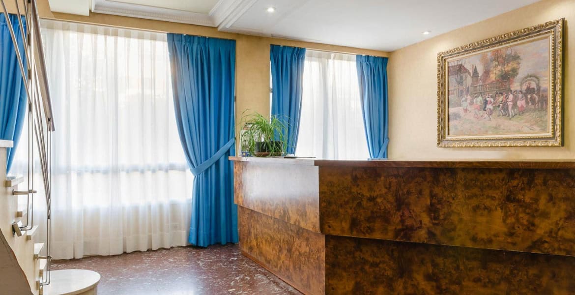 Amplia habitación de hotel con ventanas luminosas, cortinas azules y decoración clásica en Madrid Río. Perfecta para estancias cómodas cerca del centro de Madrid.