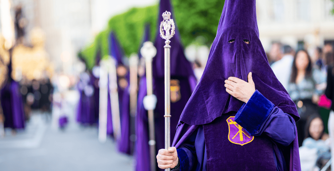 Procesión de Semana Santa en Madrid con penitentes vestido con túnicas moradas y capuchas tradicionales en la calle.