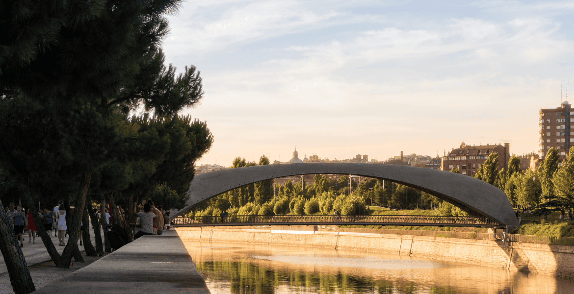Puente peatonal en el Parque Madrid Río con vistas al río Manzanares y la ciudad de Madrid al atardecer, ideal para relajarse y disfrutar de la naturaleza urbana.
