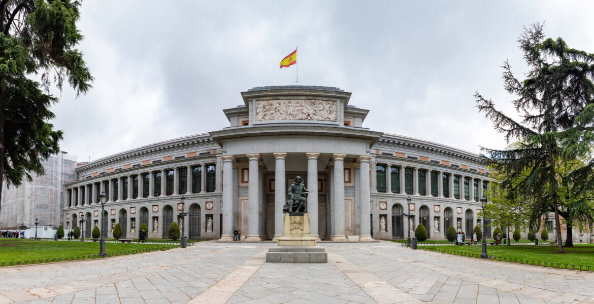 Majestuoso edificio del Parlamento de Madrid, con columnas clásicas y estatua en el frente, rodeado de jardines verdes, en el corazón de Madrid.