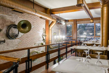 Techo de tuberías y decoración industrial en restaurante del Hotel Madrid Río, con vista a grandes ventanas y ambiente acogedor.