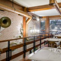 Techo de tuberías y decoración industrial en restaurante del Hotel Madrid Río, con vista a grandes ventanas y ambiente acogedor.