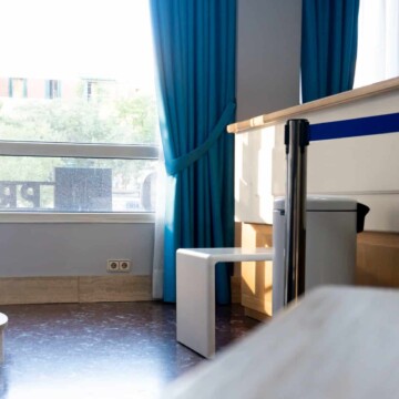 Puerta de habitación de hotel con ventana y cortinas azules, interior luminoso y cómodo en Hotel Madrid Río, ideal para viajeros que buscan alojamiento en Madrid.