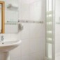 Espejo y lavabo en baño moderno del Hotel Madrid Río con duchas de cristal y azulejos blancos.