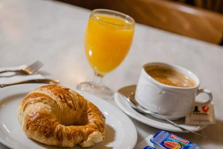 Bocadillo de cruasan junto a café y zumo de naranja en desayuno en Hotel Madrid Río, alojamiento en Madrid con desayunos gourmet.